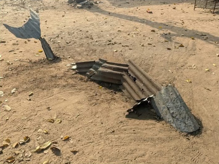 Corrugated tin whale sculpture surfacing from sand, tail raised